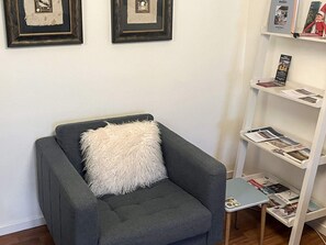A grey armchair with a fluffy white pillow, a small side table, and a bookshelf with magazines and a framed picture. - 5 Person Holiday Home in Saeby (Sæby)