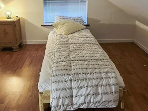 A single bed with a floral-patterned duvet in a room with wooden flooring and a window with blinds.