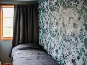 A room with a single bed, a window with curtains, and a wall with a floral pattern.