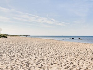 A sandy beach with footprints leading to the water, a flag on the left, and a clear sky. - 5 Person Holiday Home in Falkenberg (Falkenberg)