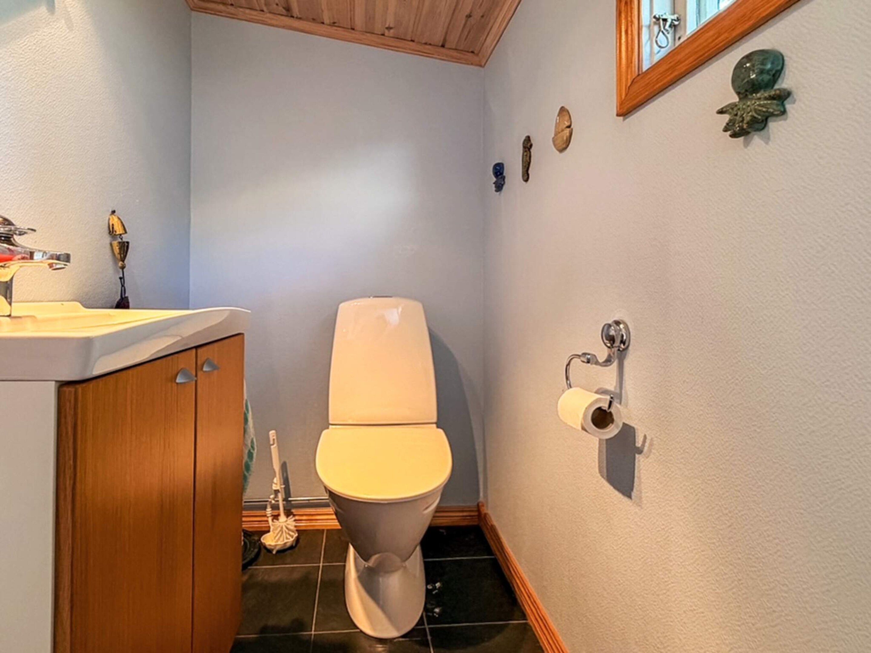 A bathroom with a toilet, sink, and wooden cabinet.