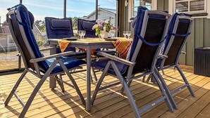 Eine überdachte Terrasse mit Tisch und Stühlen, großen Fenstern und Blick auf die Nachbarschaft.