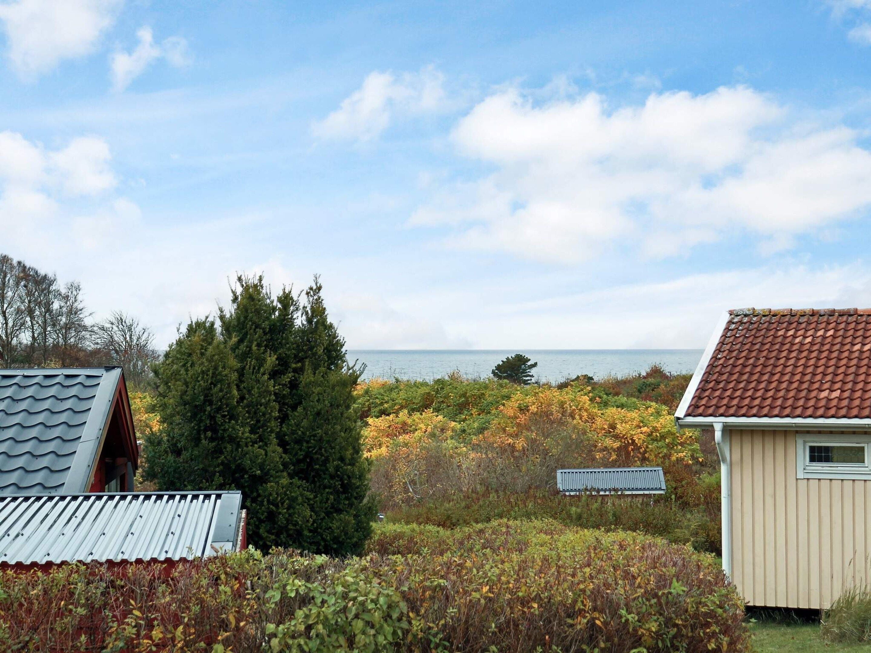 A coastal property with a view of the sea, surrounded by vegetation and two buildings with distinct roofing styles.