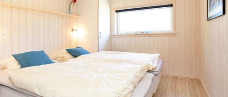 A bedroom with a bed, a wardrobe, a window, and wooden walls.