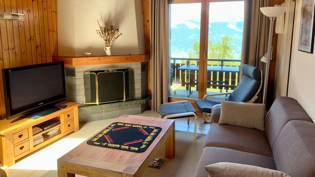 A cozy living room with a fireplace, a television, a sofa, and a balcony with a view of the mountains. - Apartment in Veysonnaz Near Ski Lift (Sion)