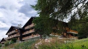 A multi-story wooden chalet with balconies, surrounded by lush greenery and trees. - Apartment in Veysonnaz Near Ski Lift (Sion)