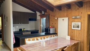 A wooden interior with a kitchen, dining area, and a view of the outdoors. - Apartment in Veysonnaz Near Ski Lift (Sion)