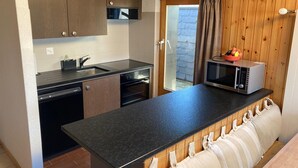 A compact kitchen with dark wooden cabinets, a black countertop, a built-in microwave, and a small sink. - Apartment in Veysonnaz Near Ski Lift (Sion)