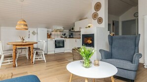 Een moderne woonkamer met een open haard, een eethoek met een houten tafel en stoelen, en een keuken op de achtergrond.