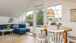 Een gezellige kamer met een blauwe bank, een ronde houten tafel met witte stoelen en een hangende rieten lamp.