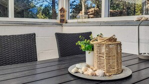 Een overdekt terras met rieten meubels, een tafel met decoratieve objecten en uitzicht op de omgeving.