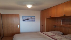 Ein Schlafzimmer mit einem Einzelbett, einem Holzschrank und einem an der Wand befestigten Regal.