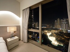 A hotel room with a night view of a cityscape, including illuminated buildings and a water feature. - New 2BR | Burj & Fountain View |Dubai Mall (Dubai)
