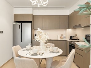 A modern kitchen with wooden cabinets, a built-in oven, and a dining area with a round table set for four. - New 2BR | Burj & Fountain View |Dubai Mall (Dubai)