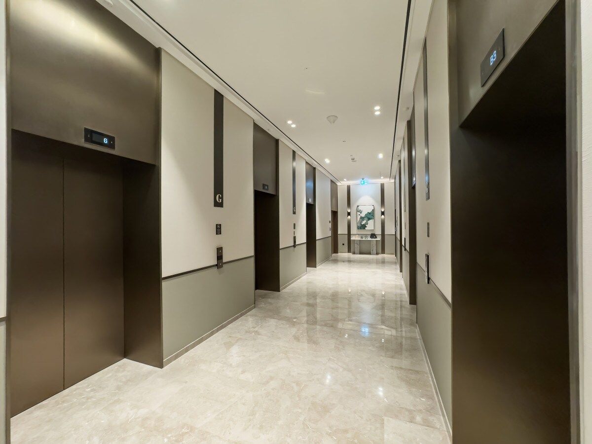 A modern hotel corridor with elevators, a polished marble floor, and a neutral color scheme.