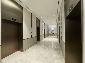 Een moderne hotelgang met liften, een gepolijste marmeren vloer en een neutraal kleurenpalet.