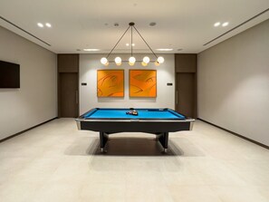A pool table in a room with a modern design, featuring recessed lighting and abstract artwork on the walls.