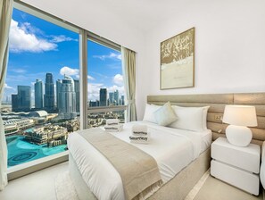 Ein Hotelzimmer mit Blick auf die Stadt, ein Bett mit weißer Bettwäsche, ein Nachttisch mit einer Lampe und ein gerahmtes Kunstwerk an der Wand.