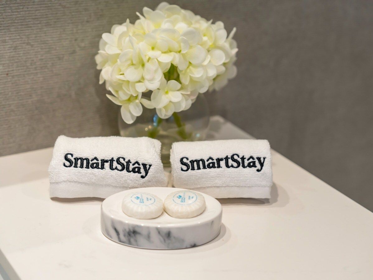 Two towels with 'SmartStay' embroidered on them, a marble tray with two soap dishes, and a vase with white flowers.