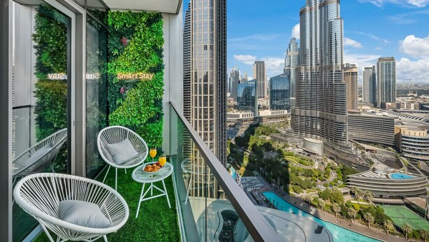 Un balcón con dos sillones blancos de mimbre, una mesa pequeña y una pared verde con plantas.