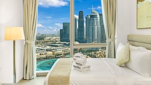 Habitación de hotel con un ventanal amplio que ofrece vistas panorámicas de la ciudad, una cama con ropa blanca y un perchero con toallas de la marca.