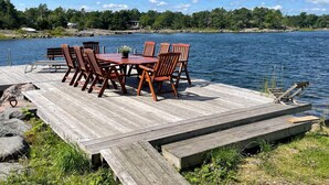 A wooden dock with a table and chairs, overlooking a calm lake with a forested shoreline. - 9 Person Holiday Home in Figeholm (Figeholm)