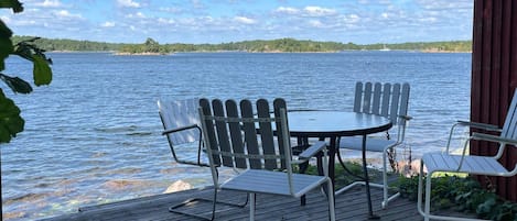 A wooden deck with a round table and four Adirondack chairs overlooking a body of water.