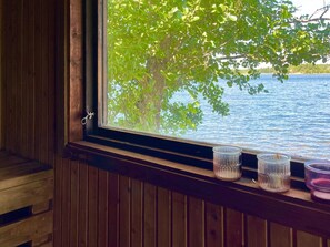 A wooden cabin with a window overlooking a lake and trees. - 9 Person Holiday Home in Figeholm (Figeholm)