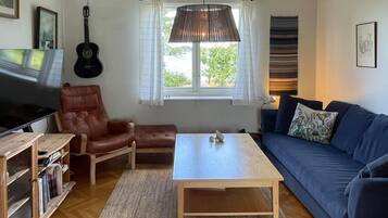 A living room with a wooden coffee table, a blue sofa, a leather armchair, a television, and a guitar.