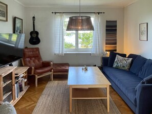 A living room with a wooden coffee table, a blue sofa, a leather armchair, a television, and a guitar. - 9 Person Holiday Home in Figeholm (Figeholm)