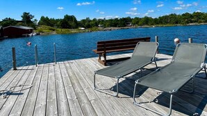 A wooden dock with two lounge chairs and a bench, overlooking a calm body of water with a clear sky. - 9 Person Holiday Home in Figeholm (Figeholm)
