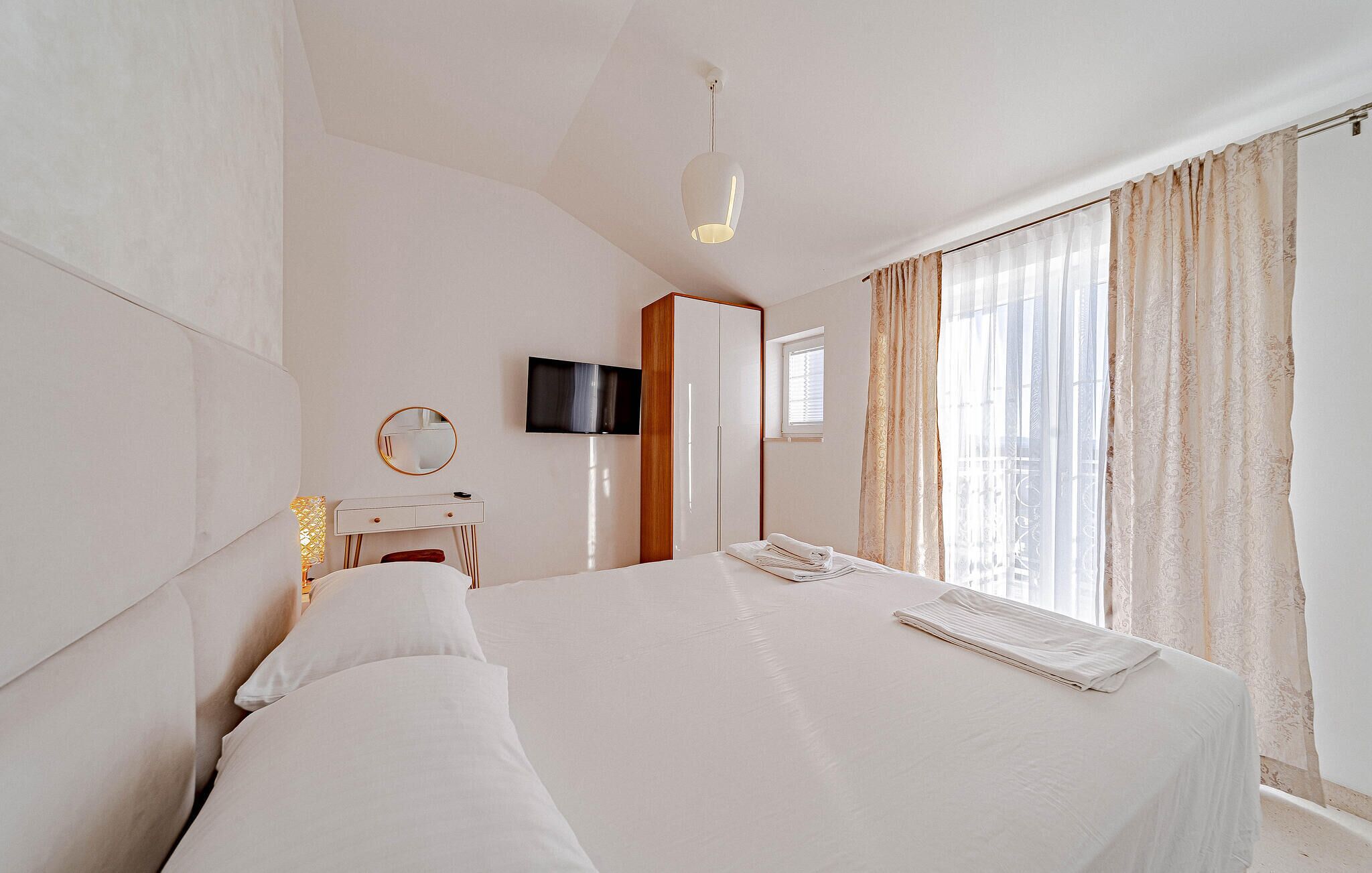 A hotel room with a bed, a TV, a wardrobe, and a window with curtains.