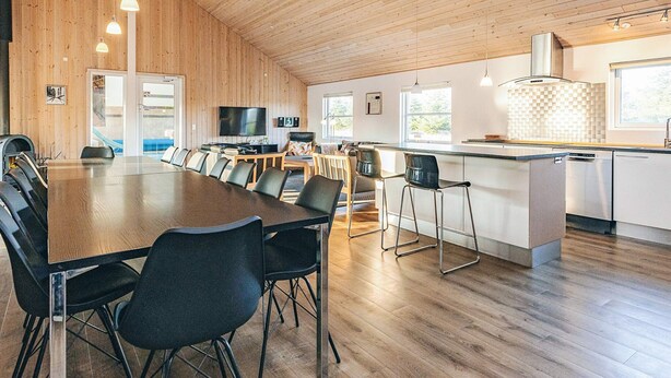 Et rummeligt køkken med træloft, et spiseområde med et langt bord og stole, samt en moderne køkkenø.