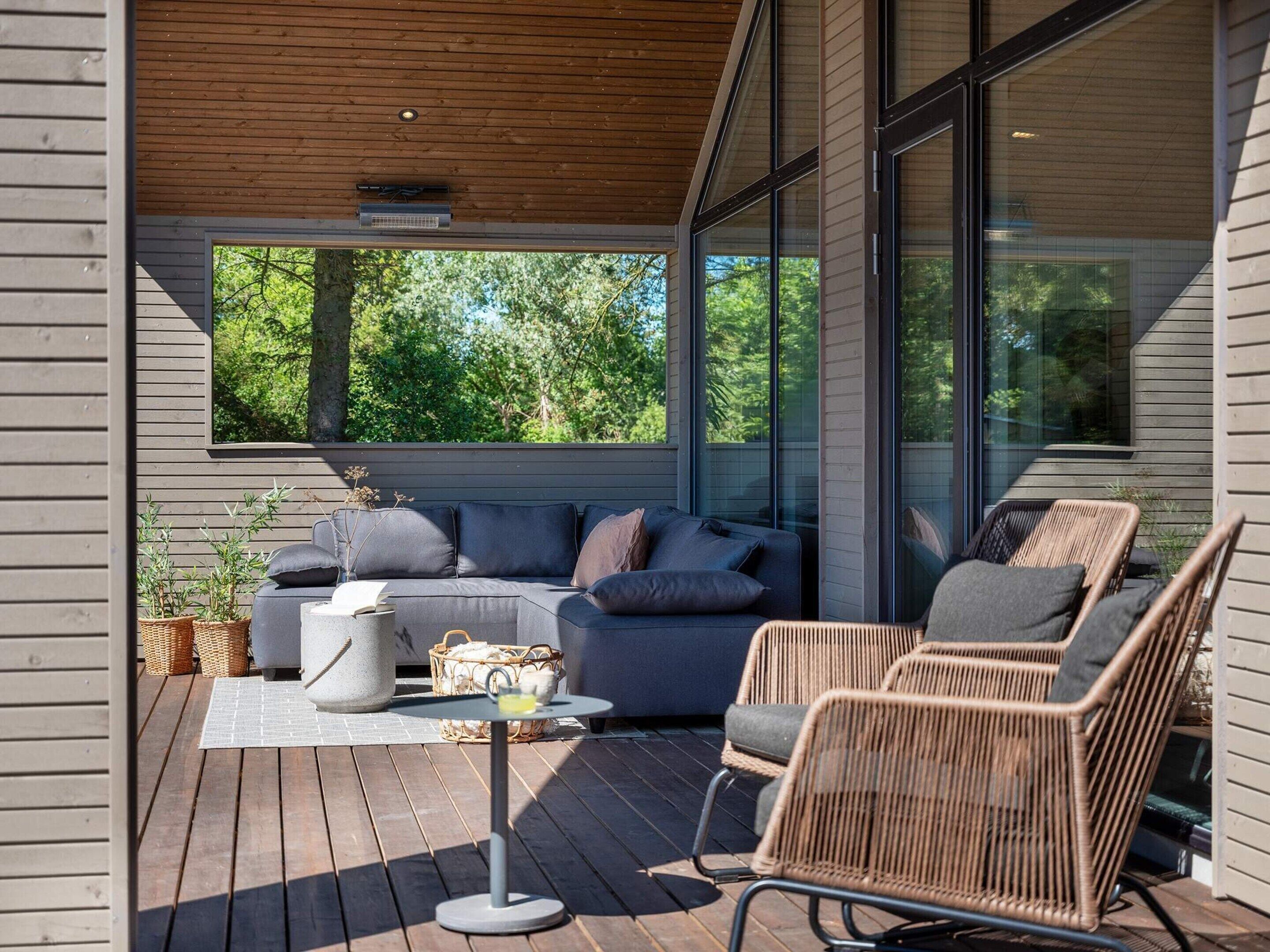 A modern outdoor seating area with a sofa and wicker chairs, a small table, and potted plants.