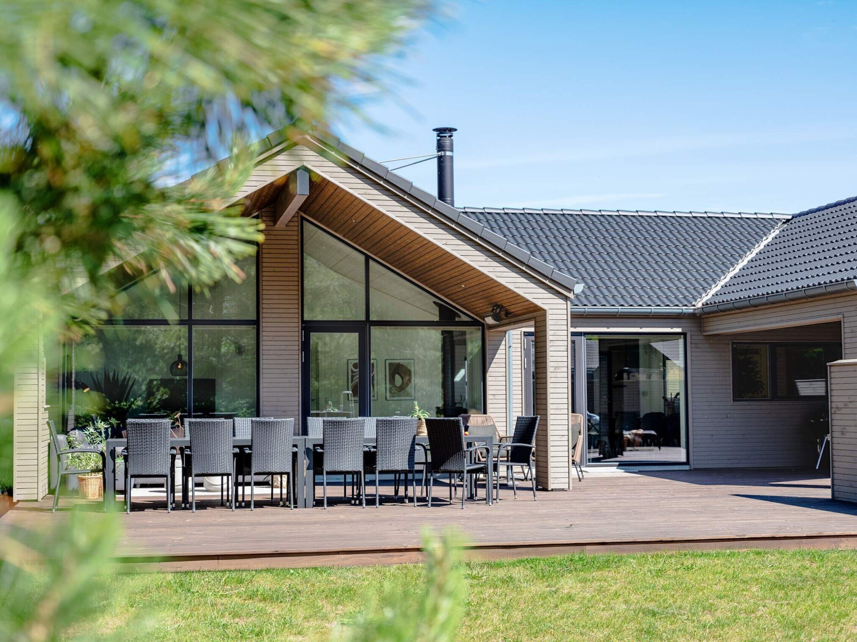 Una casa moderna con un amplio patio de cristal, mobiliario exterior y una chimenea.