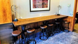 A bar area with a wooden counter, five stools, and a framed picture on the wall.