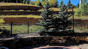 A swimming pool with a hot tub, surrounded by a stone wall and a metal fence.