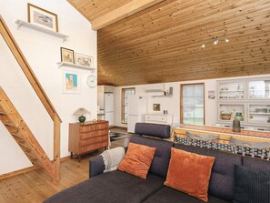 A modern living room with a wooden staircase, a sofa with cushions, a dining area with a patterned tablecloth, and a kitchen with white cabinets. - 4 Star Holiday Home in Hovborg (Hovborg)