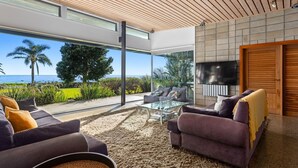 Un salon moderne doté d’une grande baie vitrée donnant sur l’océan, et aménagé avec des canapés et une table basse.