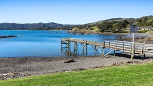 Une jetée en bois s’étendant dans un lac paisible, avec un pré verdoyant au premier plan et des collines en arrière-plan.