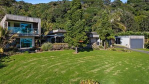 Une maison moderne à deux étages, dotée d’un balcon, entourée d’une végétation luxuriante et d’une pelouse bien entretenue.