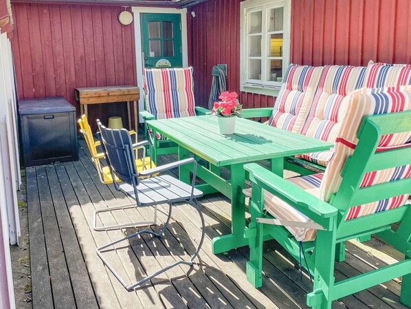 A wooden deck with a green table and chairs, a small bench, and a window with curtains. - 5 Person Holiday Home in Borgholm (Borgholm)