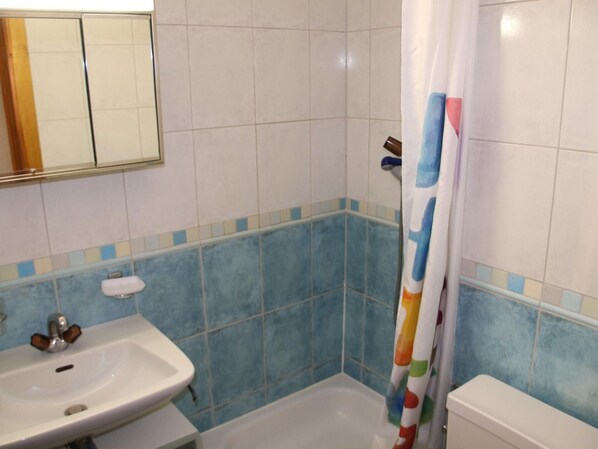 A bathroom with a white sink, blue-tiled shower area, and a white toilet. - Stunning Apartment in Heart of Valley (Veysonnaz)