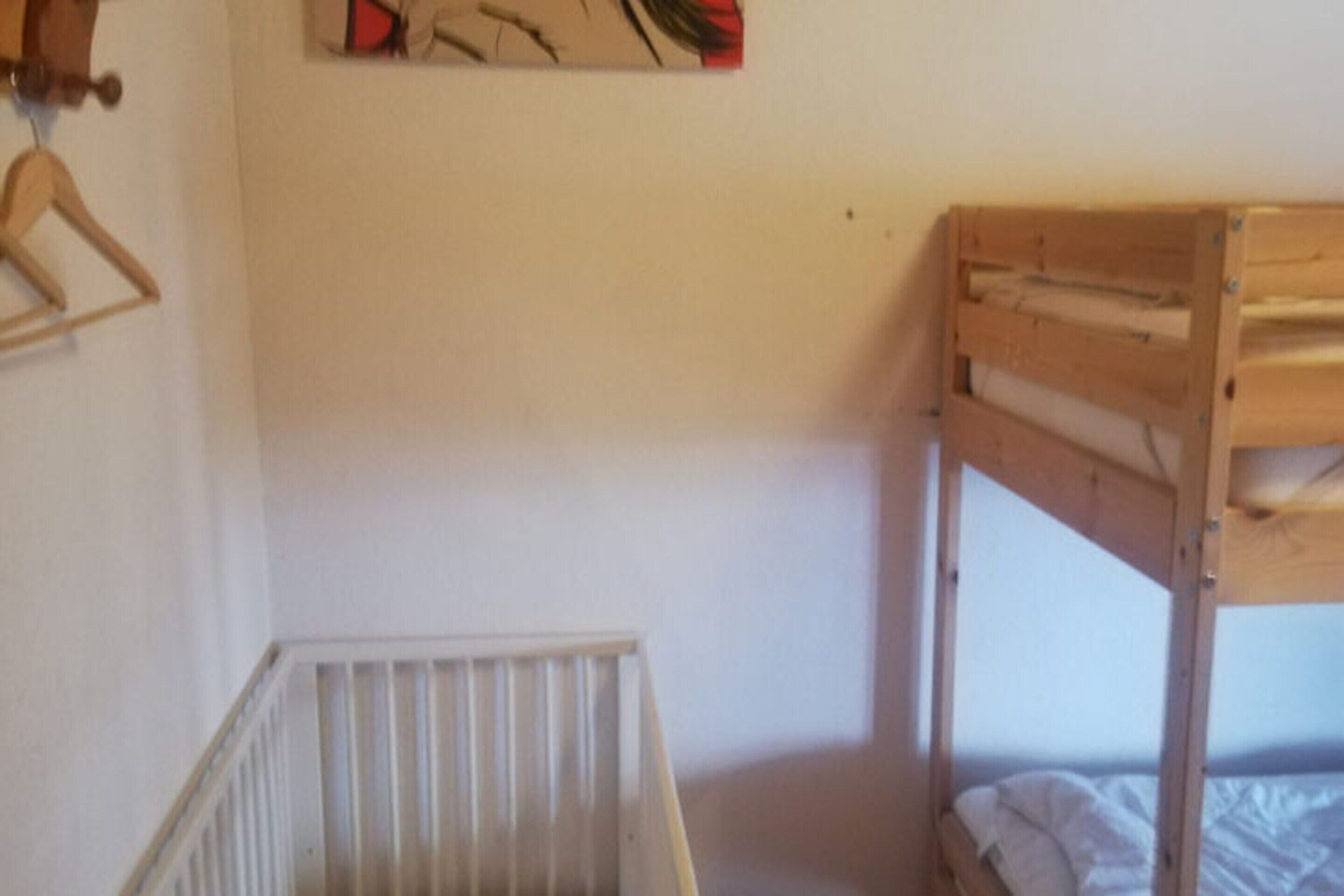 A bunk bed with a wooden headboard, a white crib, and a wooden hanger on the wall.