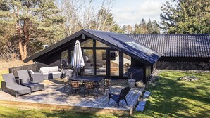 A modern outdoor patio with a dining area, seating, and a covered section. - 4 Star Holiday Home in Vaeggerlose (Vaeggerlose)