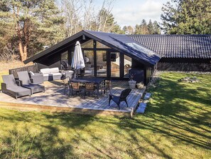 A modern outdoor patio with a dining area, seating, and a covered section. - 4 Star Holiday Home in Vaeggerlose (Vaeggerlose)