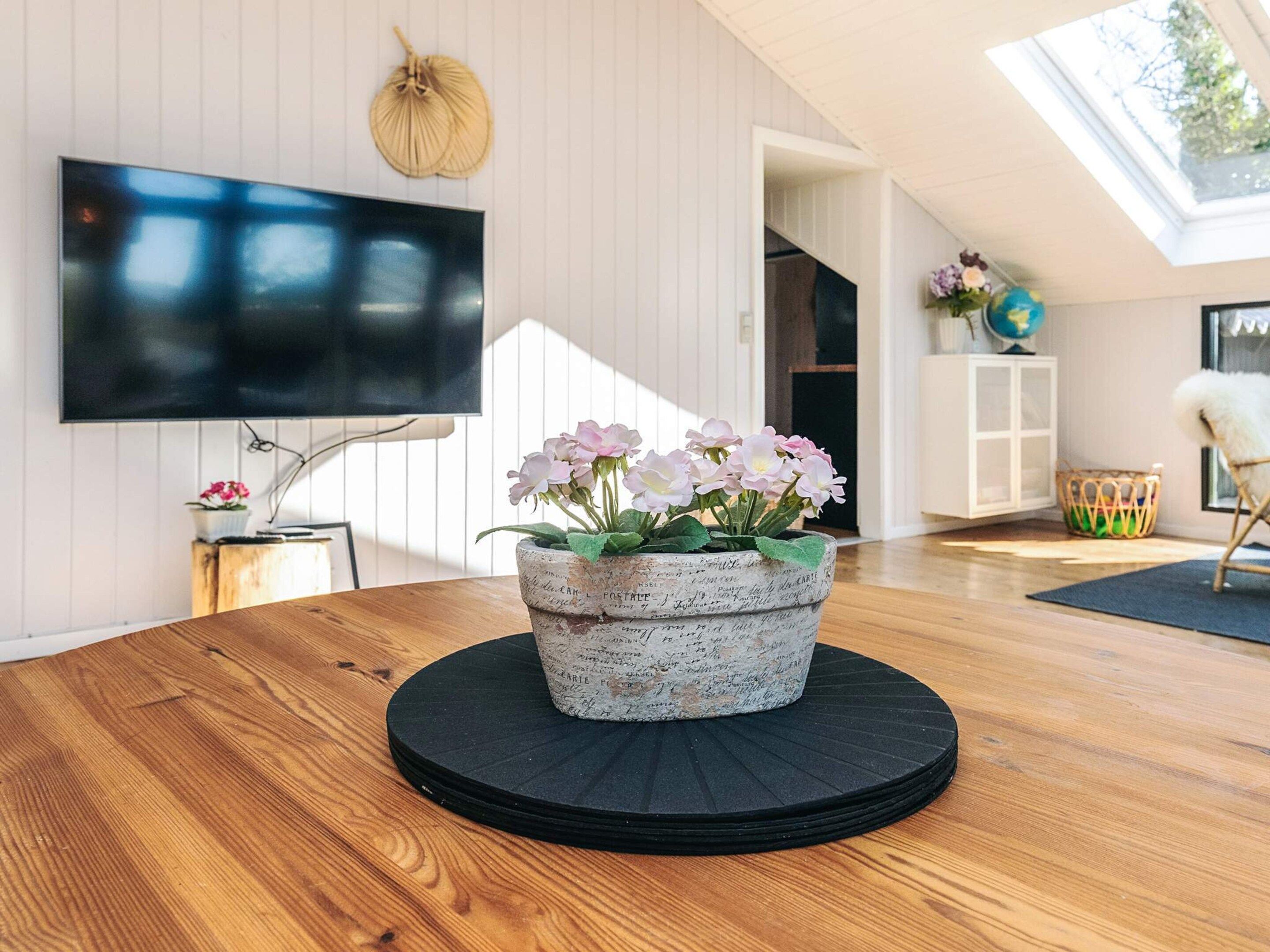 Un salon moderne avec une table en bois, un pot de fleurs décoratif en pierre, un téléviseur à écran plat et une lucarne.