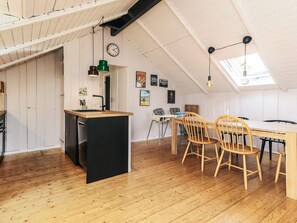 A loft-style room with a kitchen area, wooden dining table, and chairs. - 4 Star Holiday Home in Vaeggerlose (Vaeggerlose)
