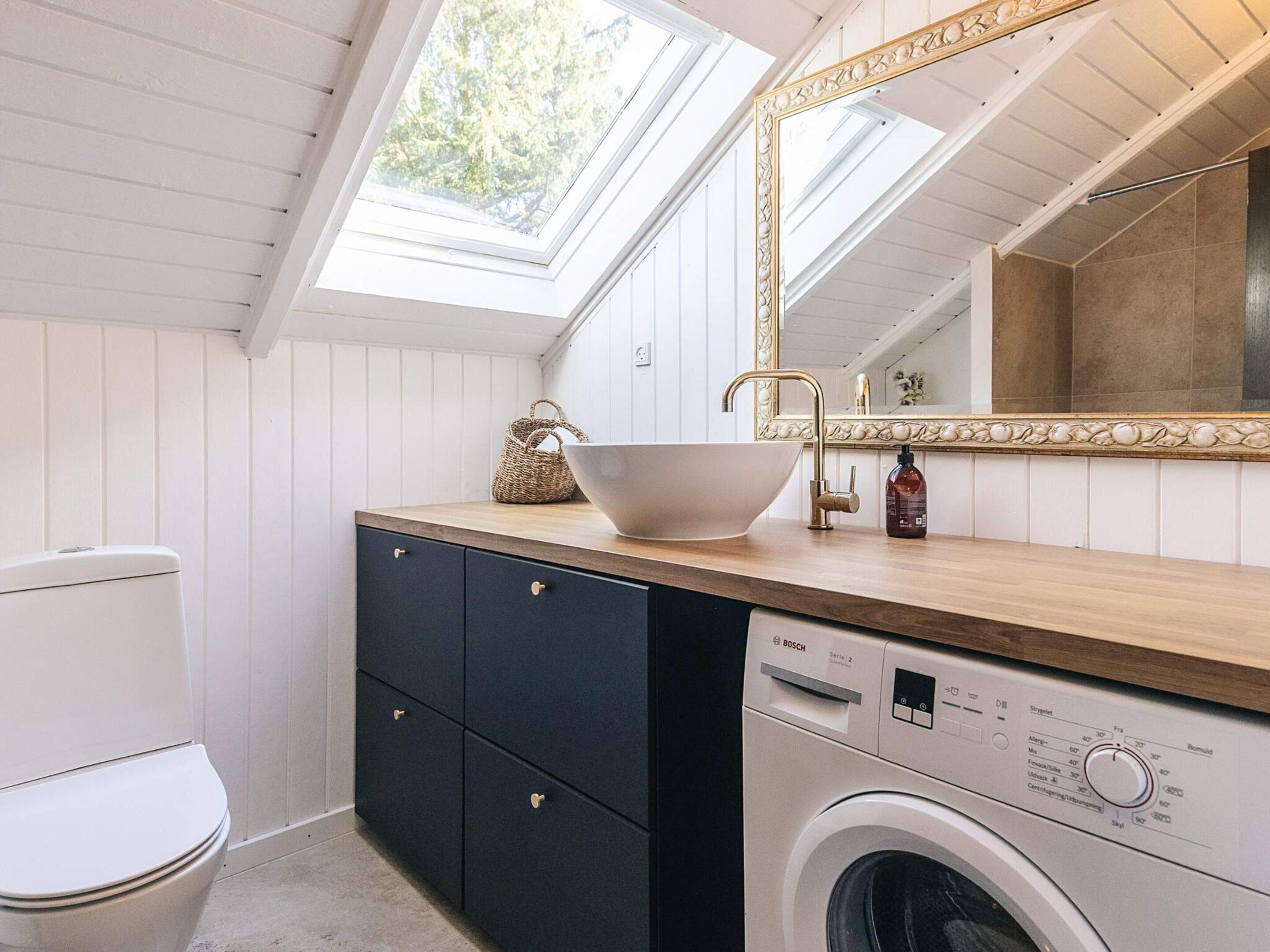 A compact bathroom with a built-in washing machine, a sink with a vessel basin, and a large mirror.