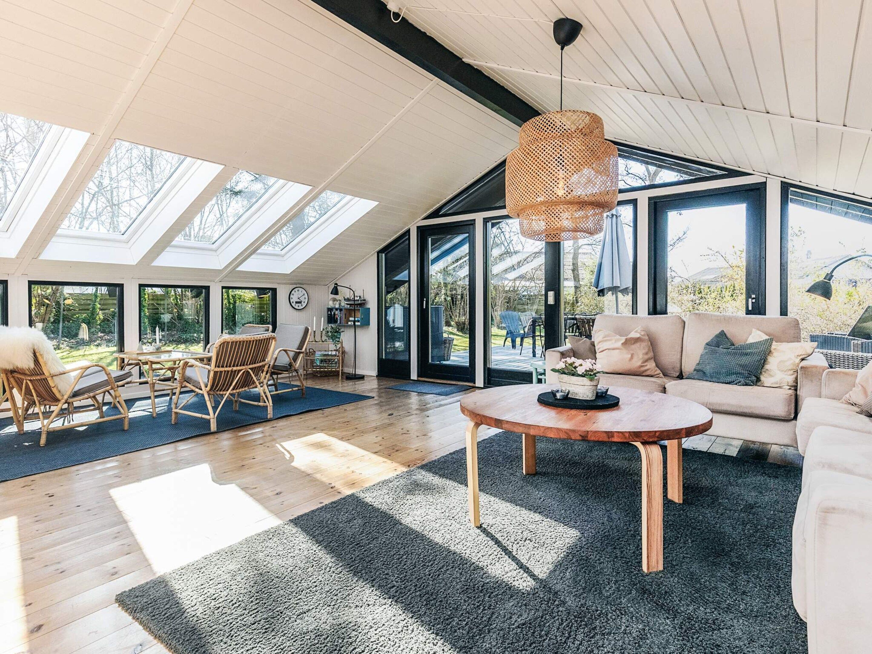 A spacious living area with a high ceiling, large windows, and a wooden coffee table. - 4 Star Holiday Home in Vaeggerlose (Vaeggerlose)